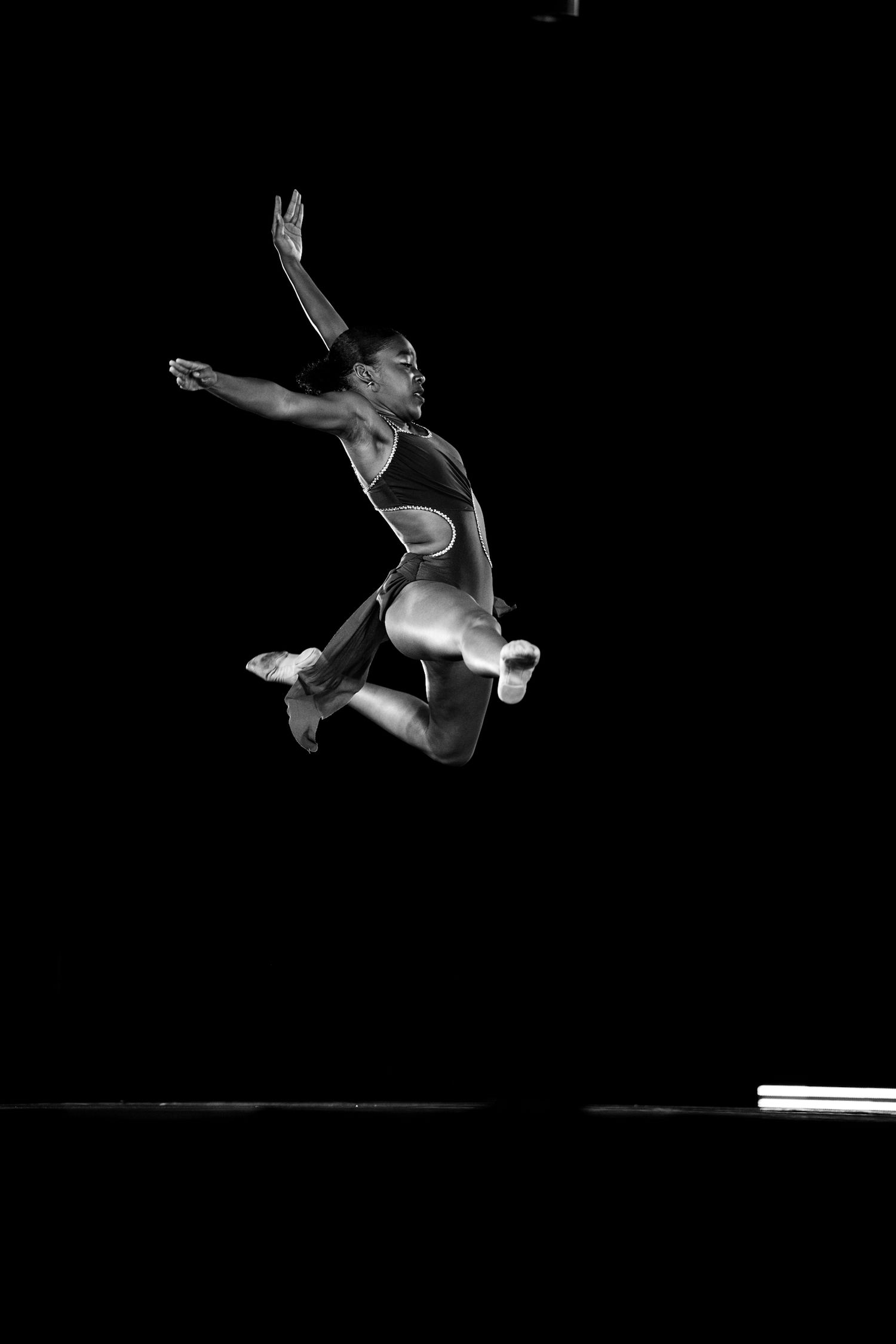 Black and white photo of a gymnast mid-air performing a dynamic leap against a dark background.