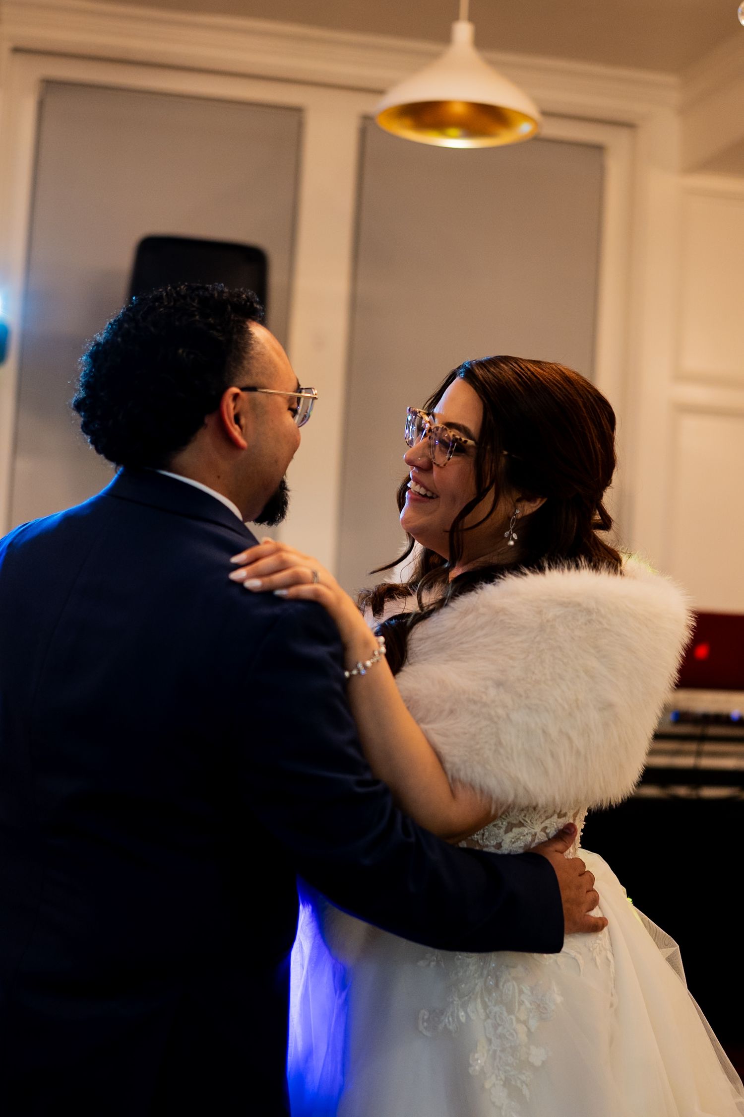 Bride in fur wrap and groom share an intimate first dance under warm indoor lighting.