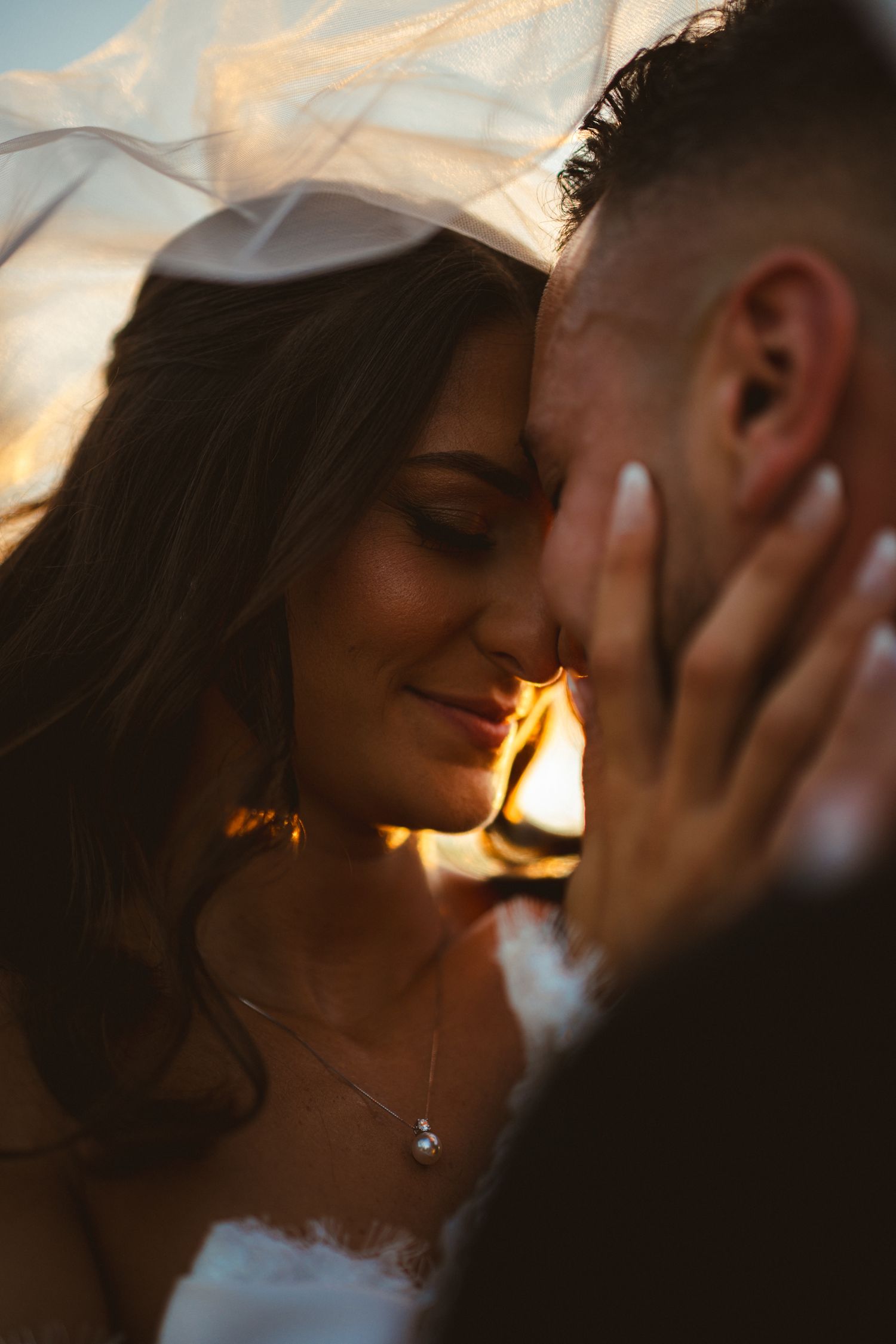 Bride and groom share an intimate moment under a veil during a golden hour sunset wedding photo.