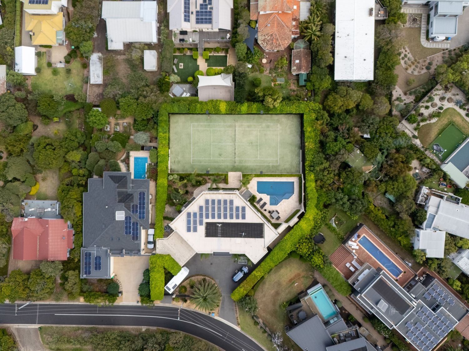 Drone image of large home with pool and tennis court, showing expansive landscaped grounds and estate layout.