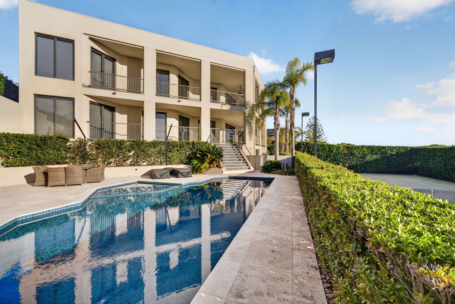 Shot from pool area showing a large house and tennis court, capturing expansive outdoor living, landscaped grounds, and resort-style ameniti
