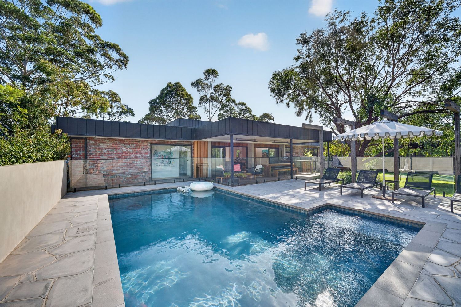 Exterior architectural image showing the rear of a house and swimming pool area, highlighting the relationship between indoor and outdoor