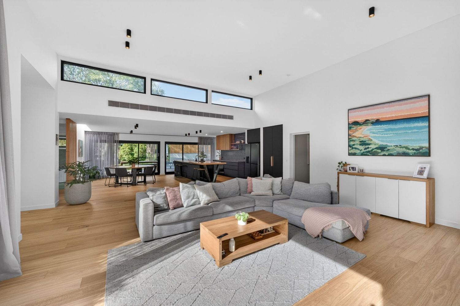 Wide shot of open-plan lounge, kitchen, and dining area, showcasing a cohesive living space with natural light, modern interior design