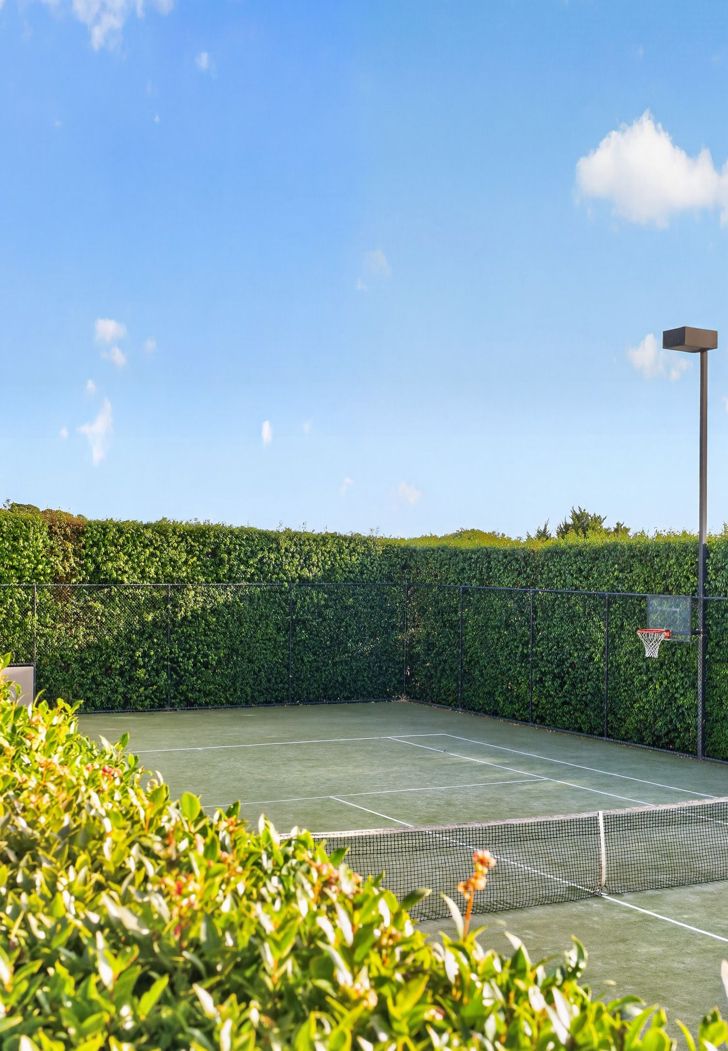 Shot of tennis court showing clean court lines, surrounding fencing, and outdoor recreational space under natural light.