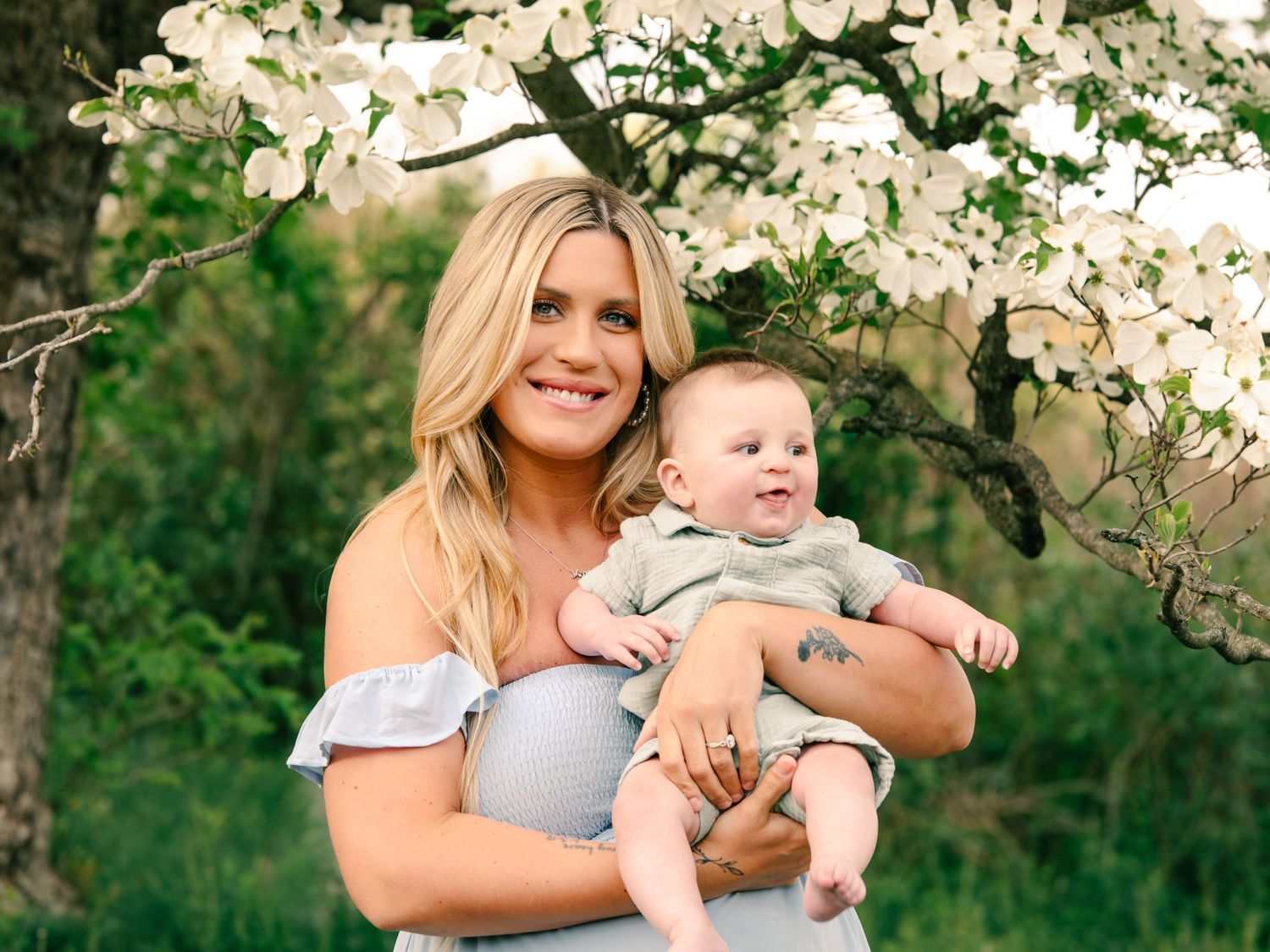 mother in blue dress holding son under flowering tree