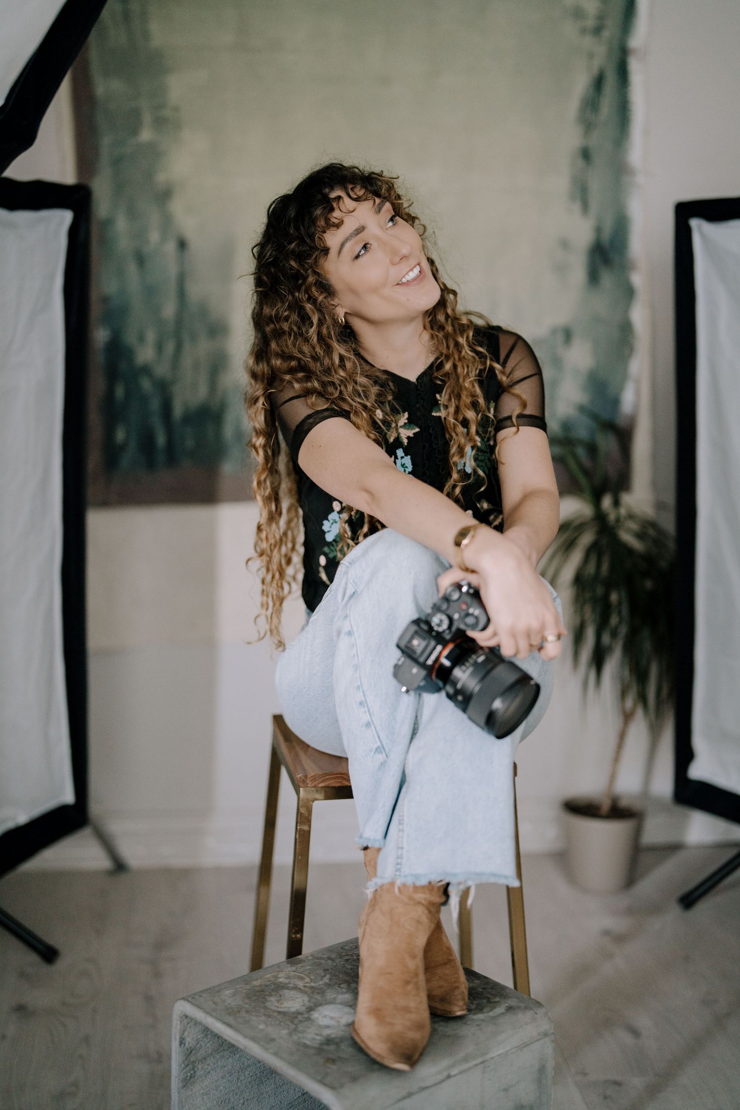 A photographer with curly hair in a white top and brown boots poses artistically across multiple dynamic shots in a studio.