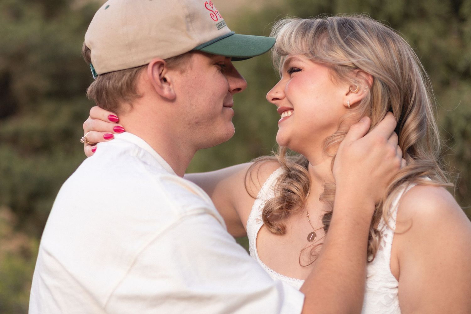 A romantic couple sharing a tender moment outdoors, the man in a green cap gently holding the womans face.