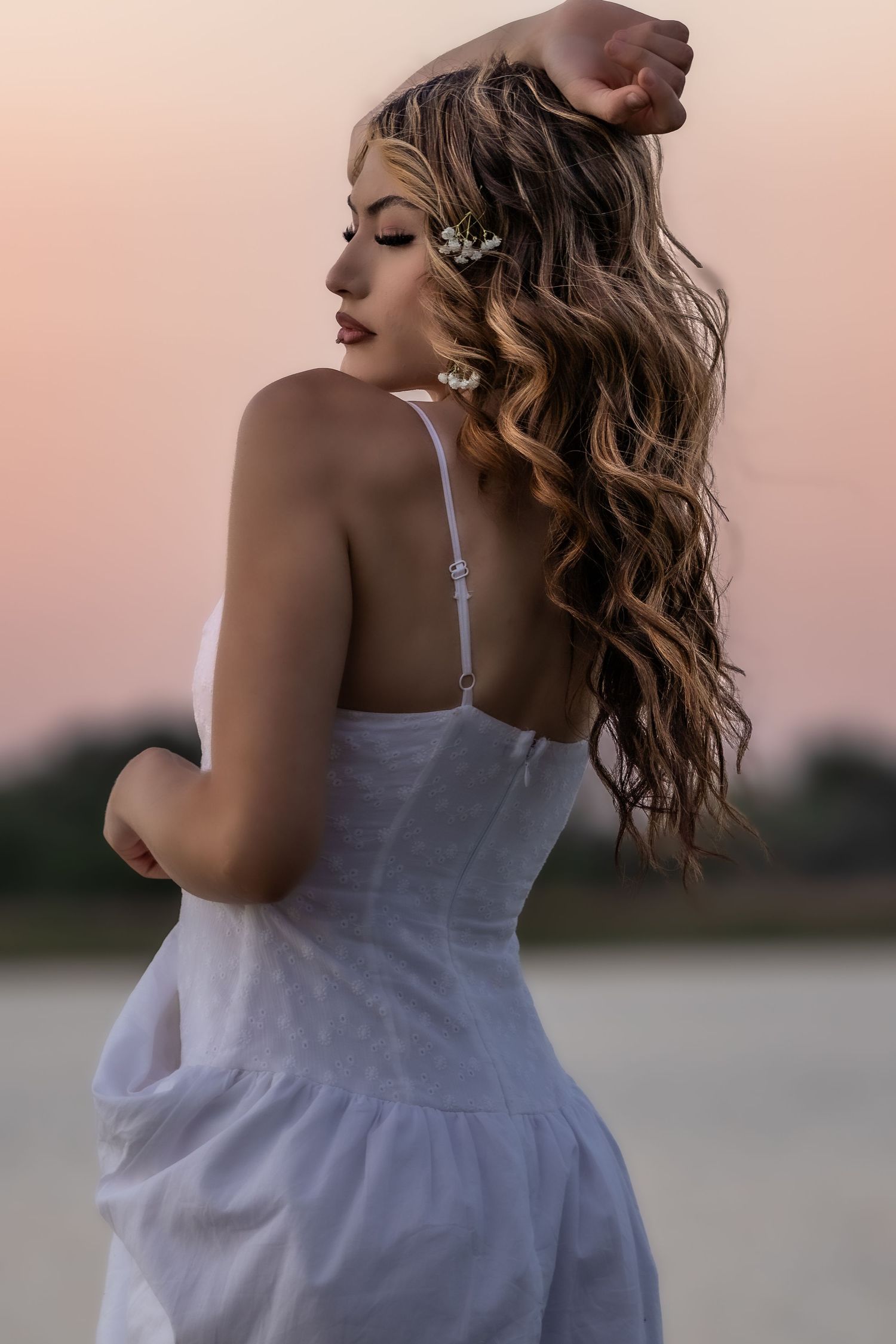 Woman in white dress with flowing wavy hair poses at sunset near water in Littleton, Colorado.