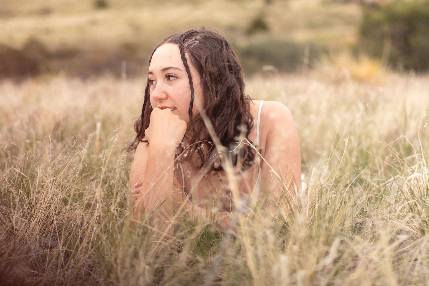 Brunette woman lying in tall grass field, looking away thoughtfully in natural lighting Littleton, Colorado.