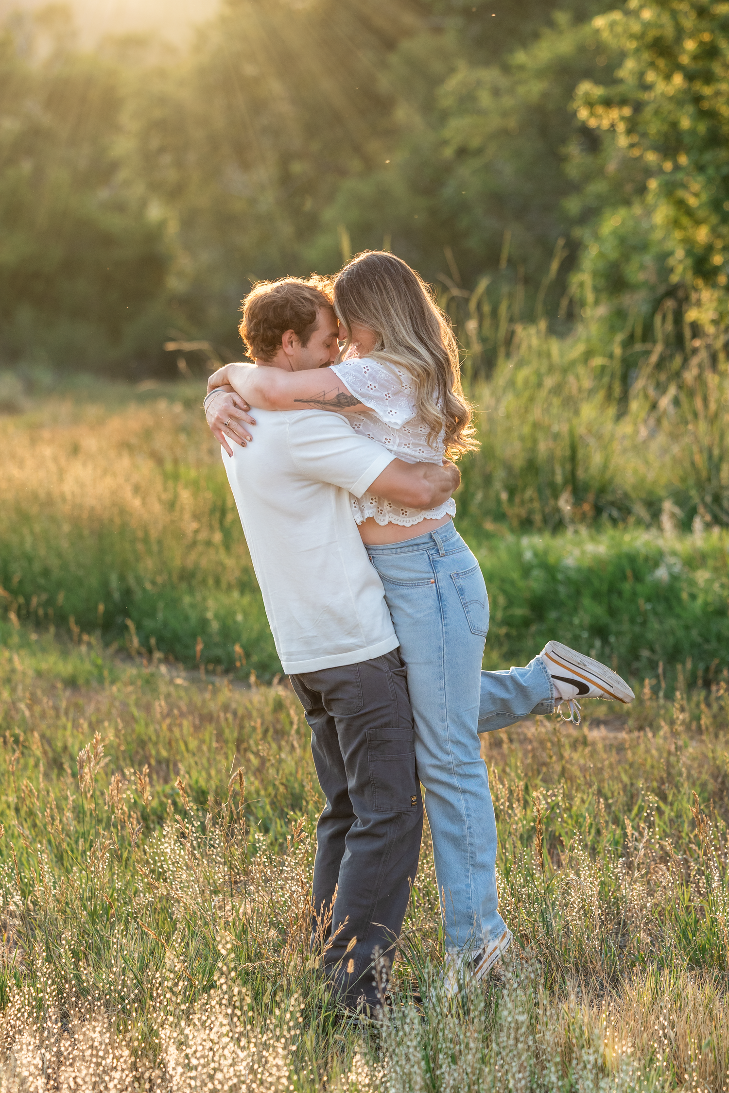 Couple embracing in a sunlit field, sharing a romantic hug surrounded by lush greenery at golden hour.