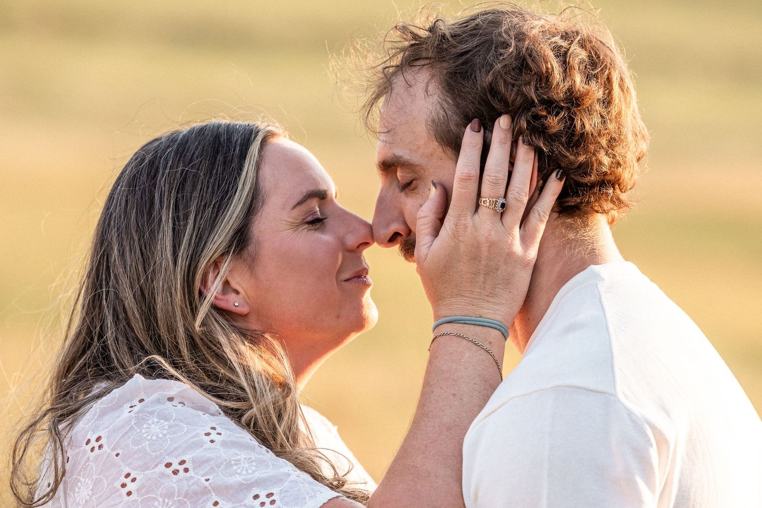 Couple sharing a romantic almost-kiss outdoors in a golden field, woman tenderly holding mans face.