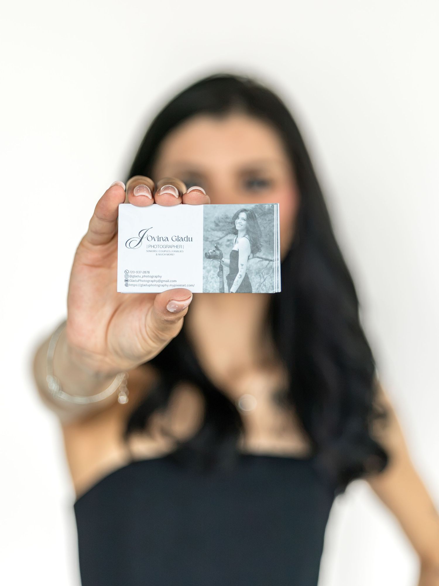 Woman with dark hair holding a business card for Jovina Giardu close to the camera in a white studio.