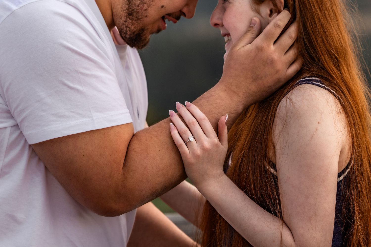 A couple shares a tender moment, man gently holding woman's face as she smiles, with her red hair cascading down.