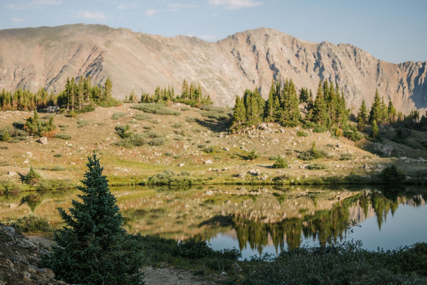 Serene alpine lake reflecting evergreen trees and rocky mountain peaks under a clear blue sky.