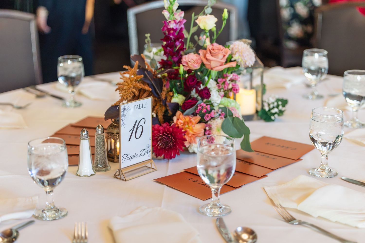 Elegant wedding reception table 16 with colorful floral centerpiece, white linens, and glassware settings.