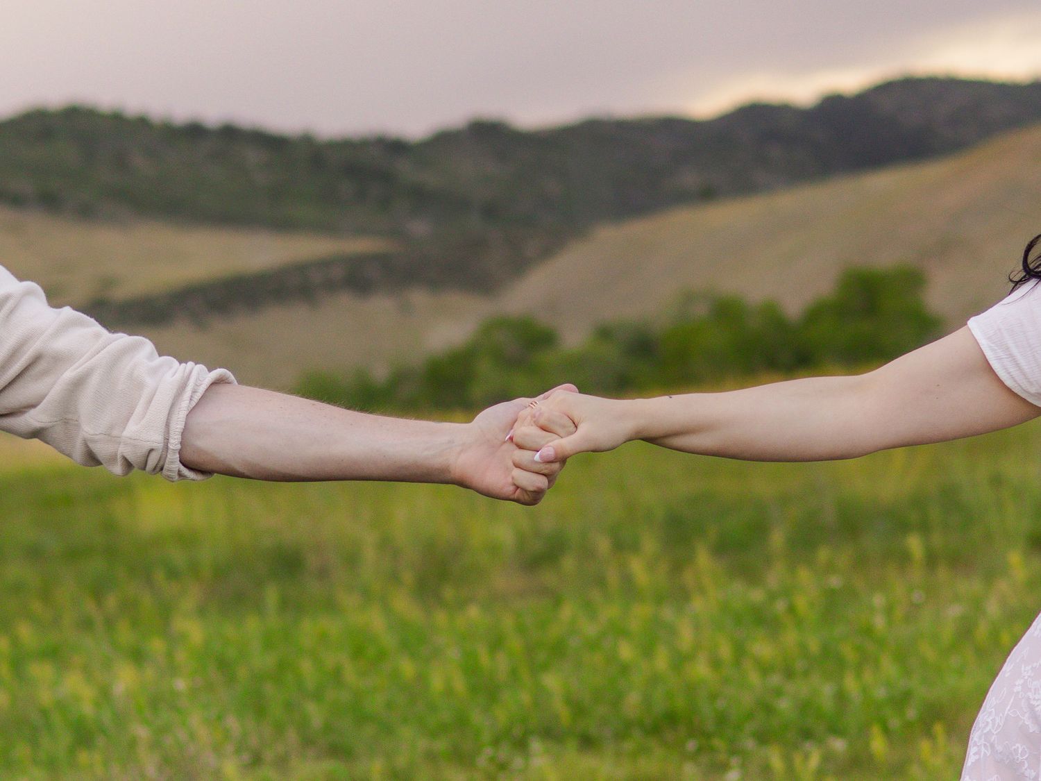 Couple holding hands in a green field with rolling hills in the background in Littleton, Colorado.