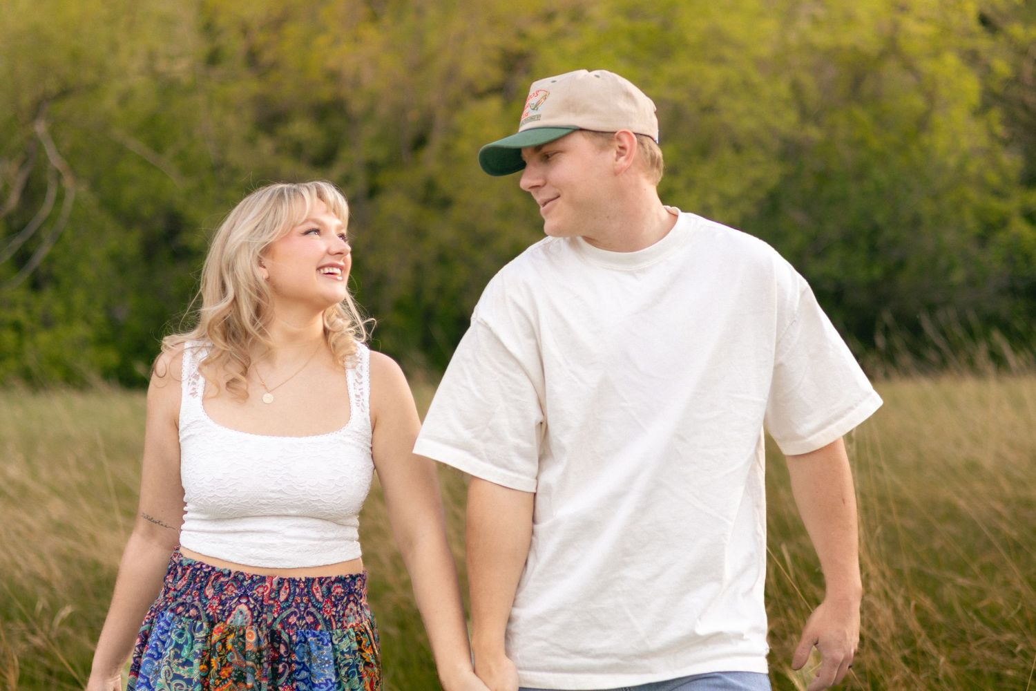 A happy young couple walking hand in hand through a golden field, smiling at each other.