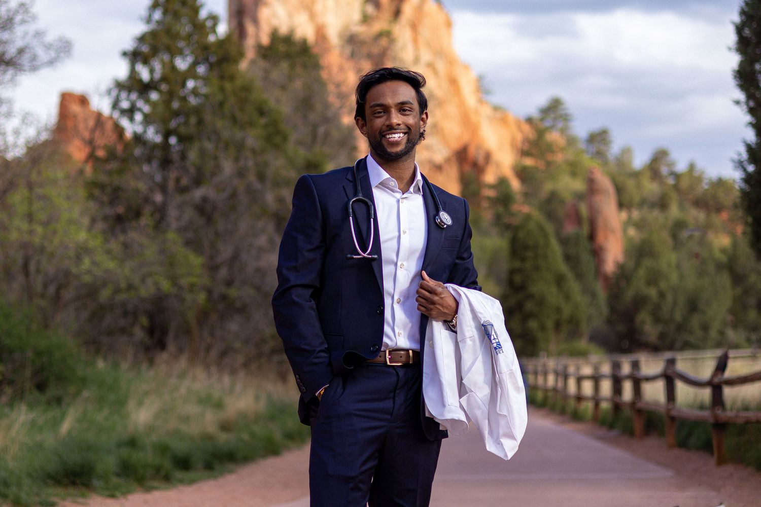 Young professional man in navy suit with stethoscope poses on scenic red rock canyon path.