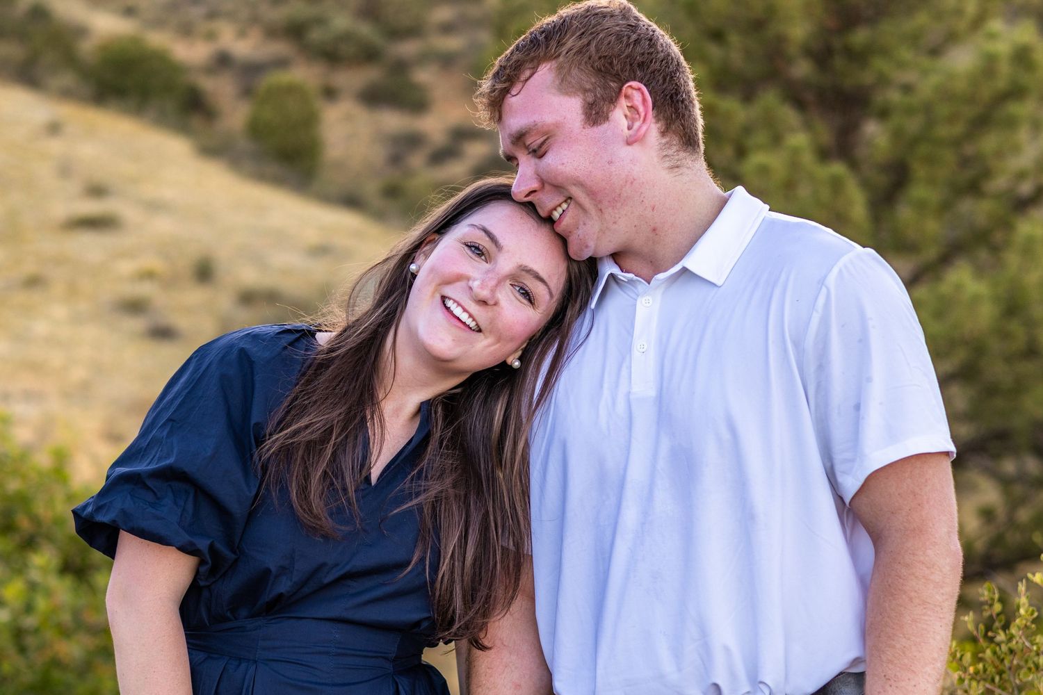 Happy couple smiling and laughing together outdoors with green hills in the background.