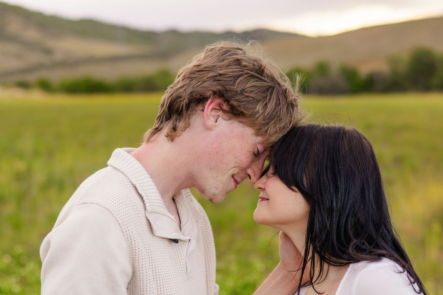 Romantic couple sharing an intimate moment in a green field with rolling hills in the background.