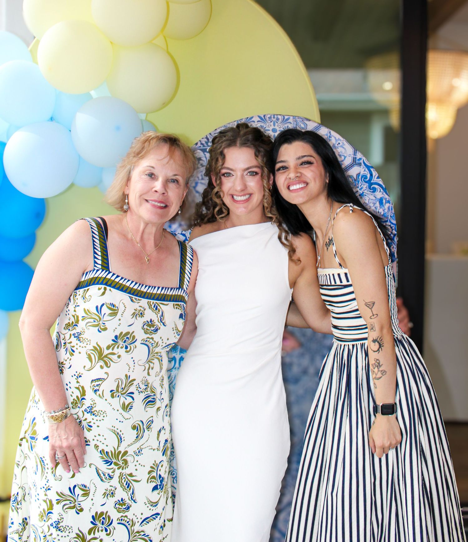 Three generations of women smile together at a festive celebration with balloon decorations.