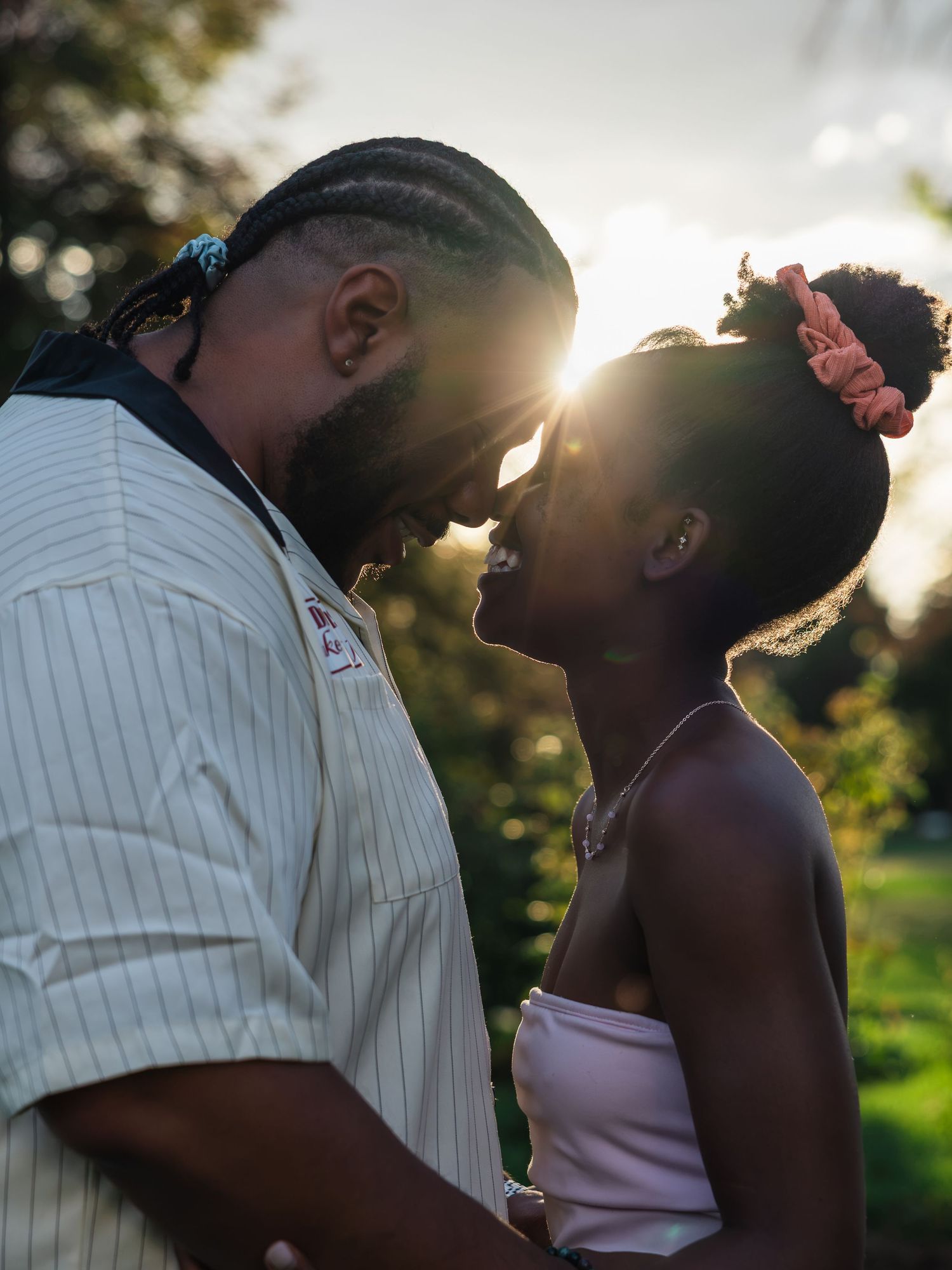 Couple sharing a romantic moment outdoors at golden hour, with sunlight glowing between them in a lush green setting.