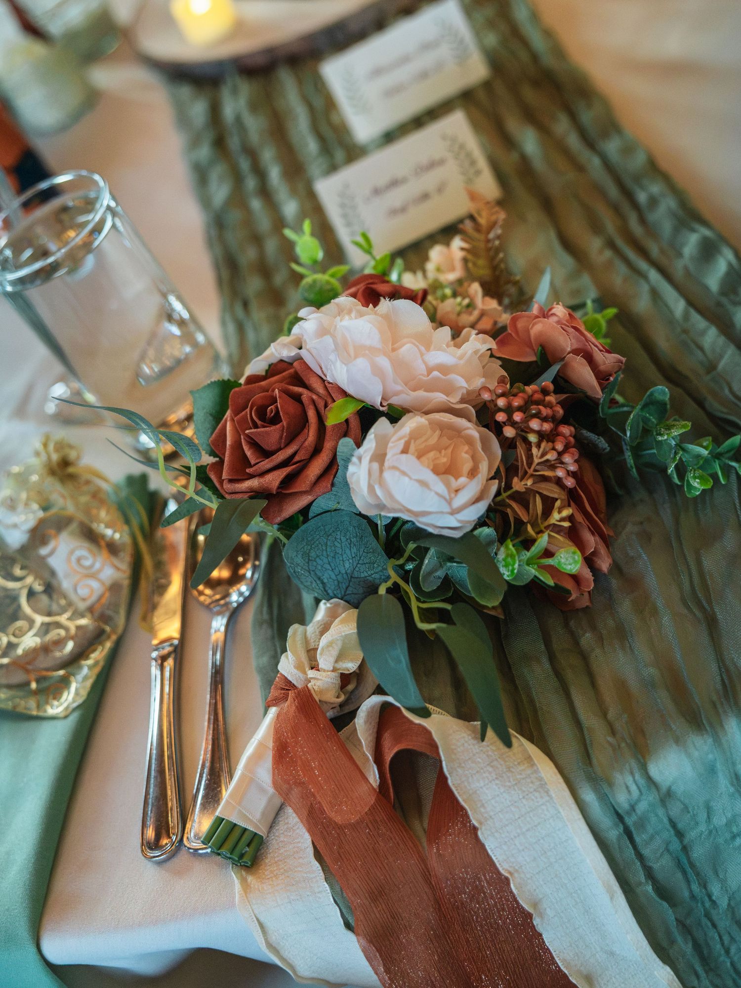 Elegant wedding table setting with dusty rose and cream floral arrangement on sage green runner with silverware.