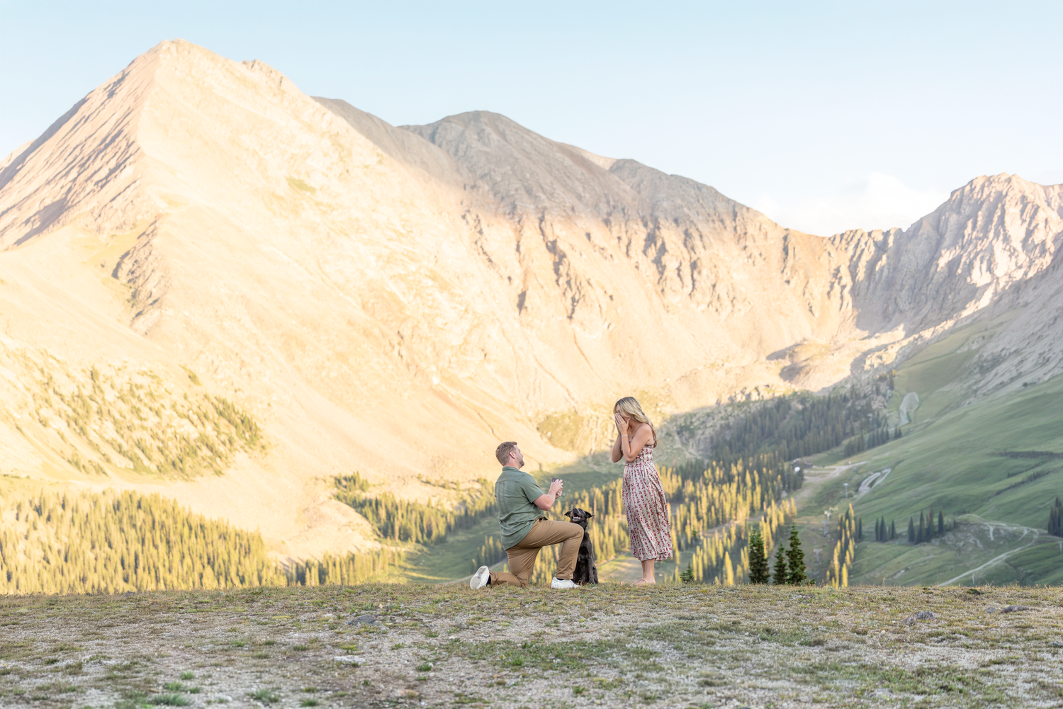 Man proposes to woman on one knee in a stunning mountain meadow at golden hour in Colorado.