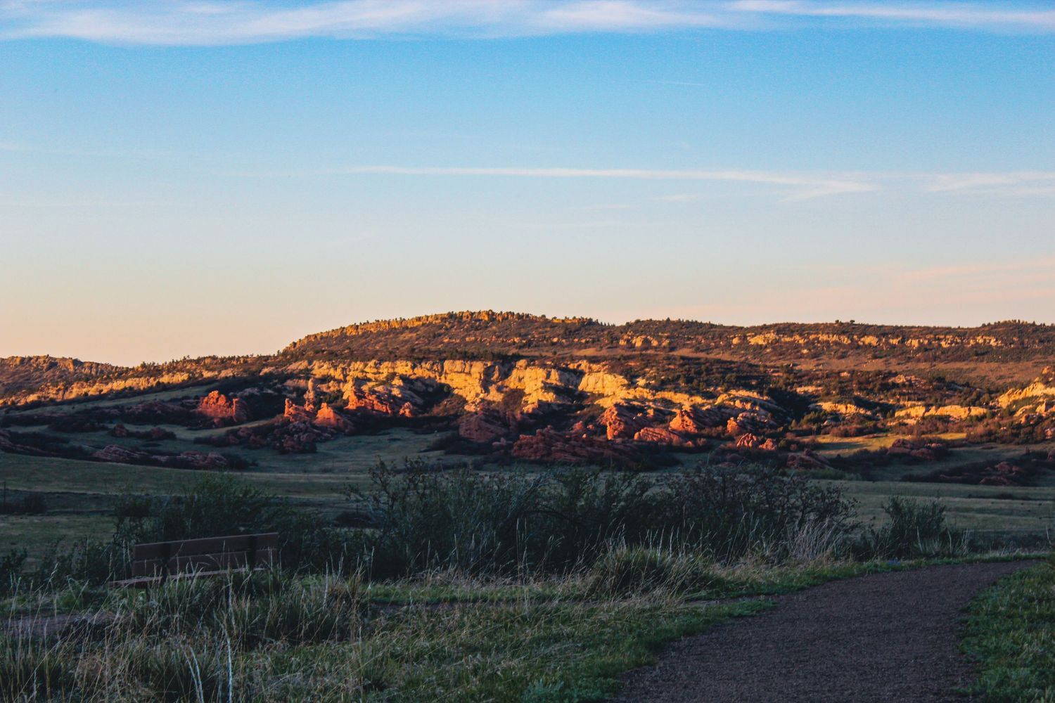 Golden hour landscape of red rock formations and rolling hills under a blue sky at dusk.
