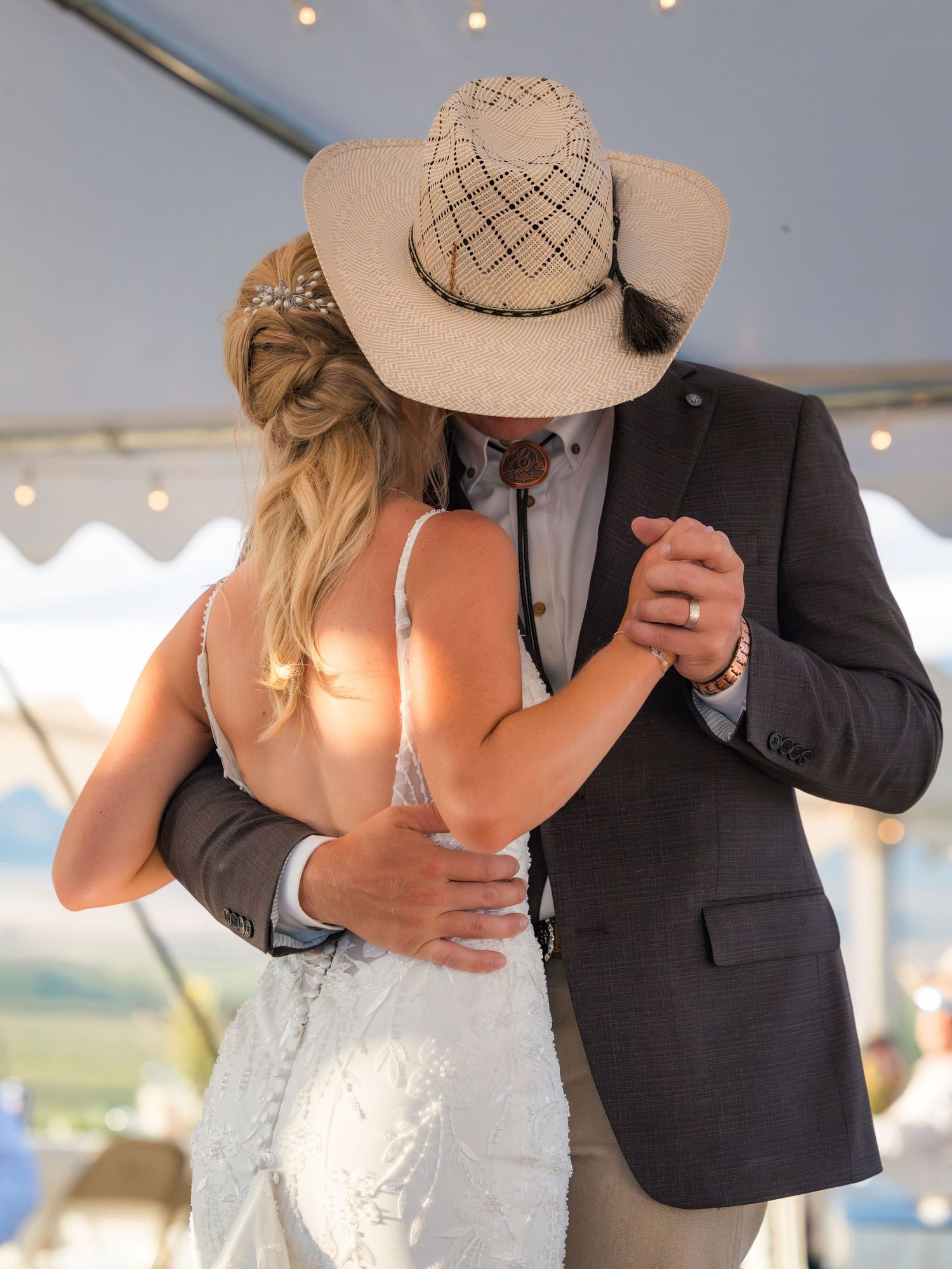 Bride and groom share first dance under tent, groom wearing cowboy hat and suit at outdoor wedding.