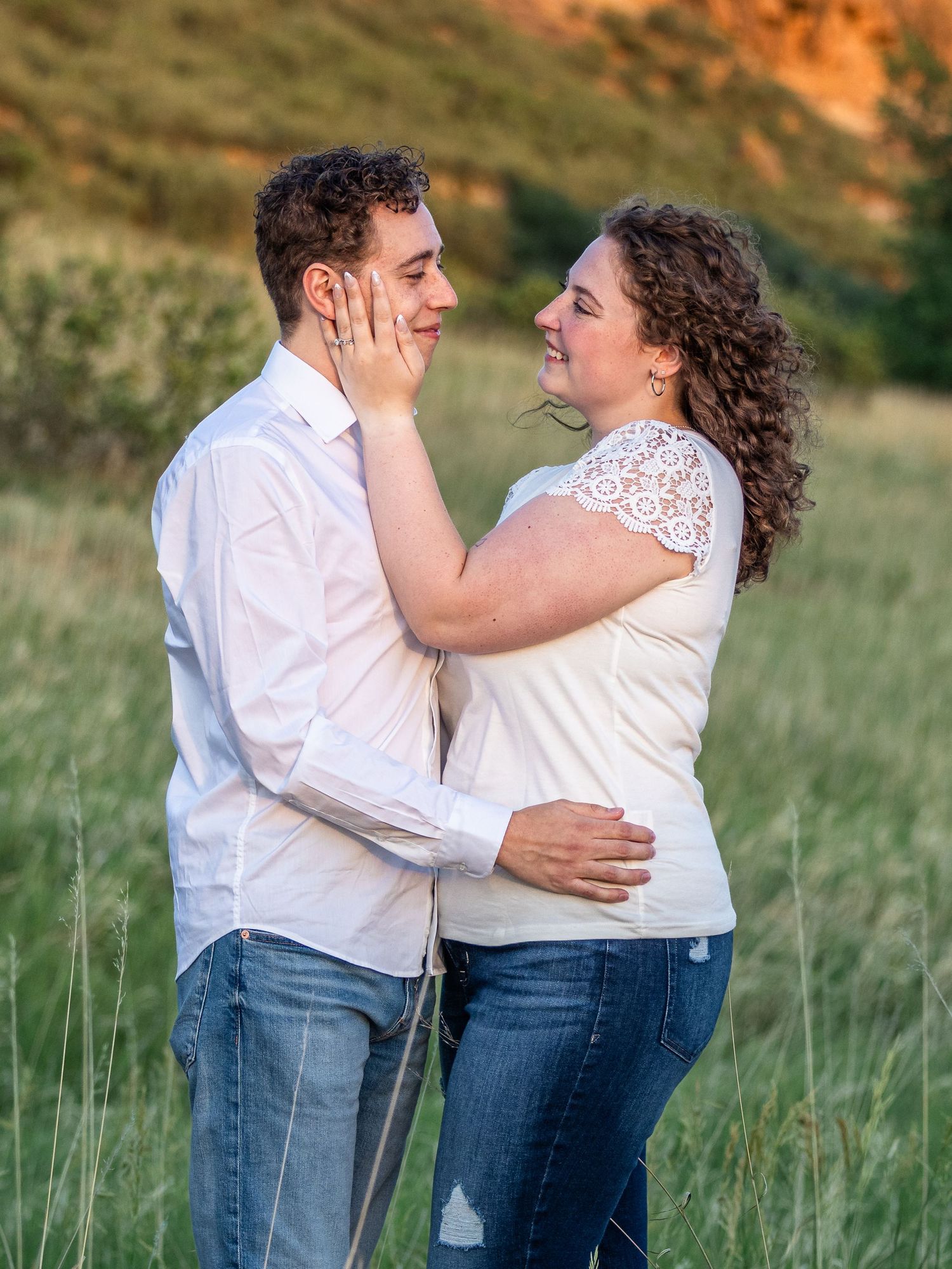 Couple sharing a tender moment in a green meadow, woman gently touching man's face, both smiling warmly.