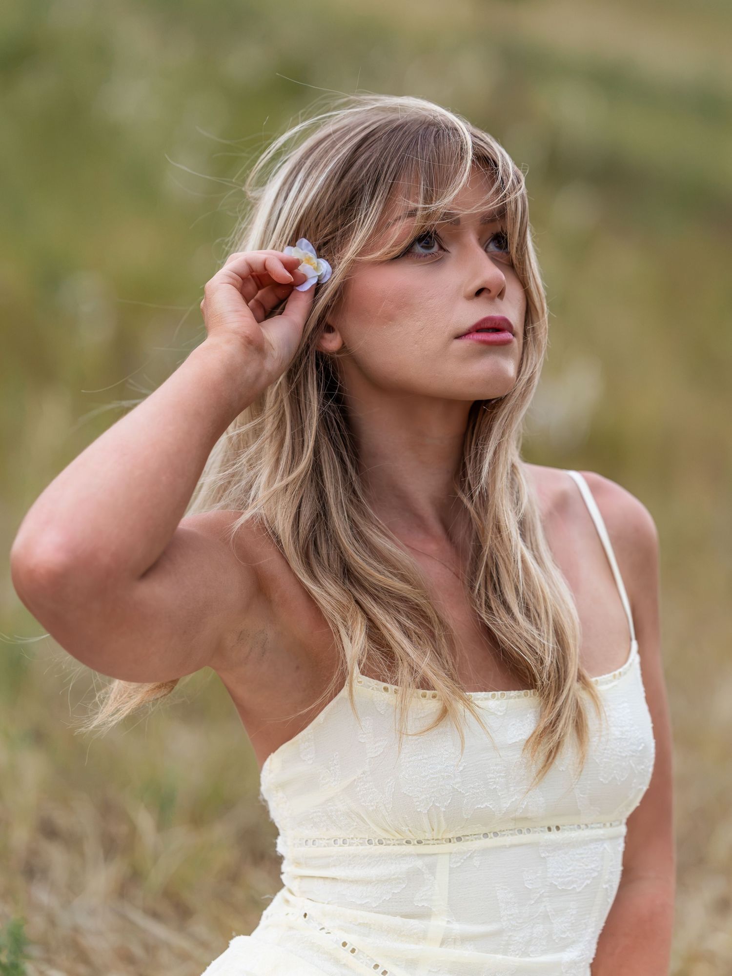 Young blonde woman in white sundress gazing upward outdoors in a natural field setting.