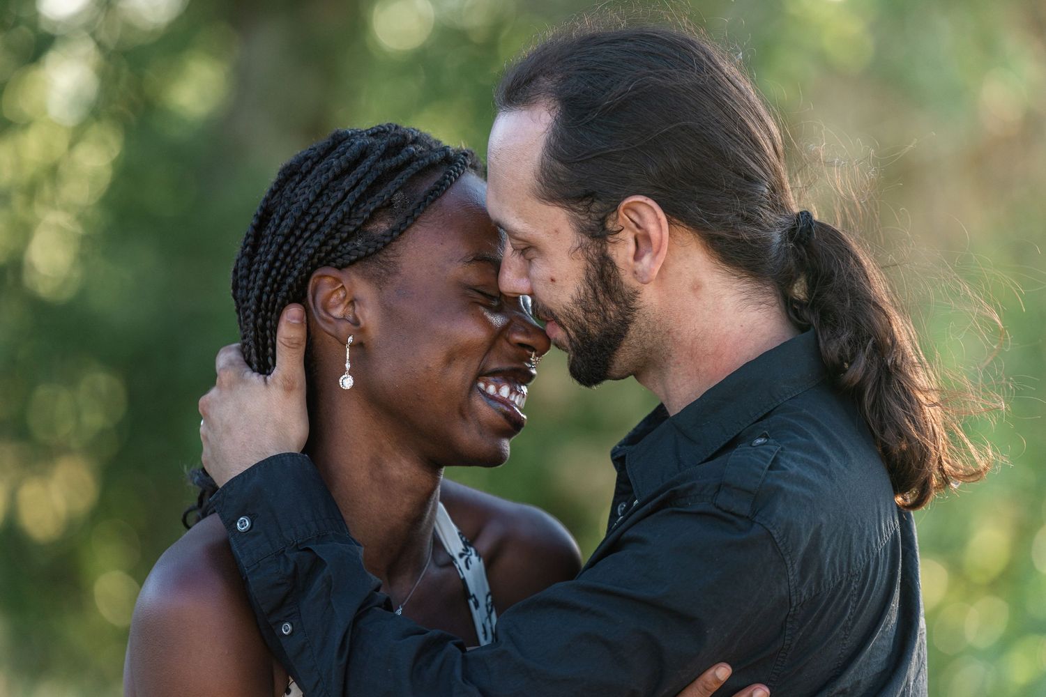 A joyful interracial couple shares a romantic moment outdoors, smiling and embracing in soft natural light.