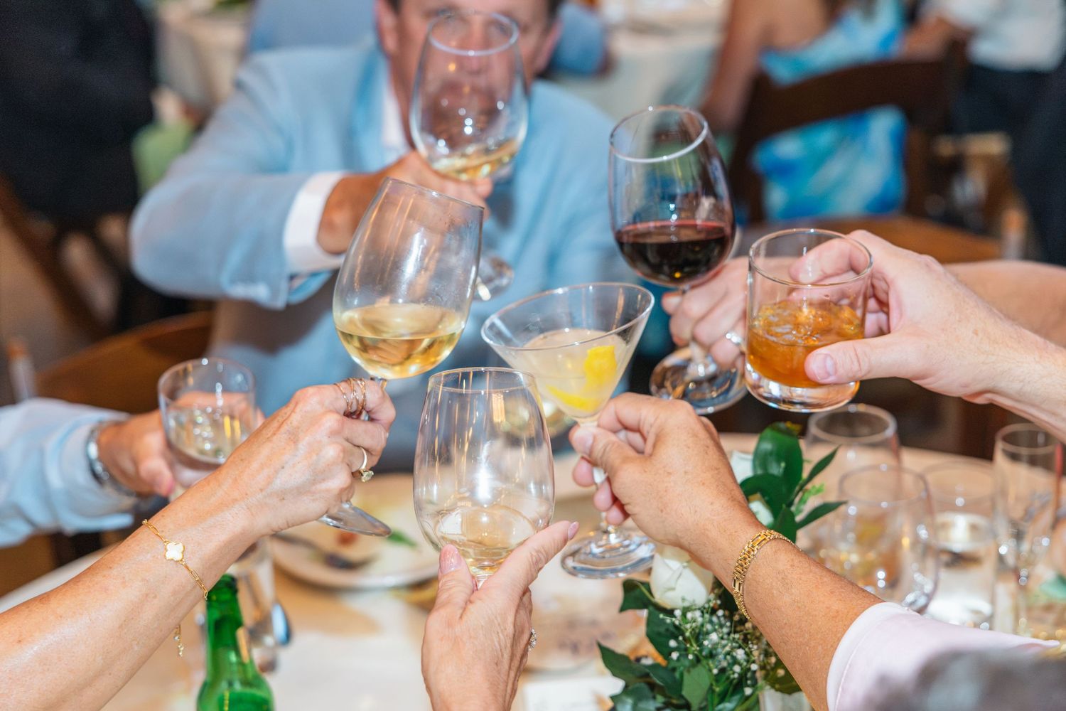 Group of people raising glasses in a celebratory toast at a formal dinner event with wine and cocktails.