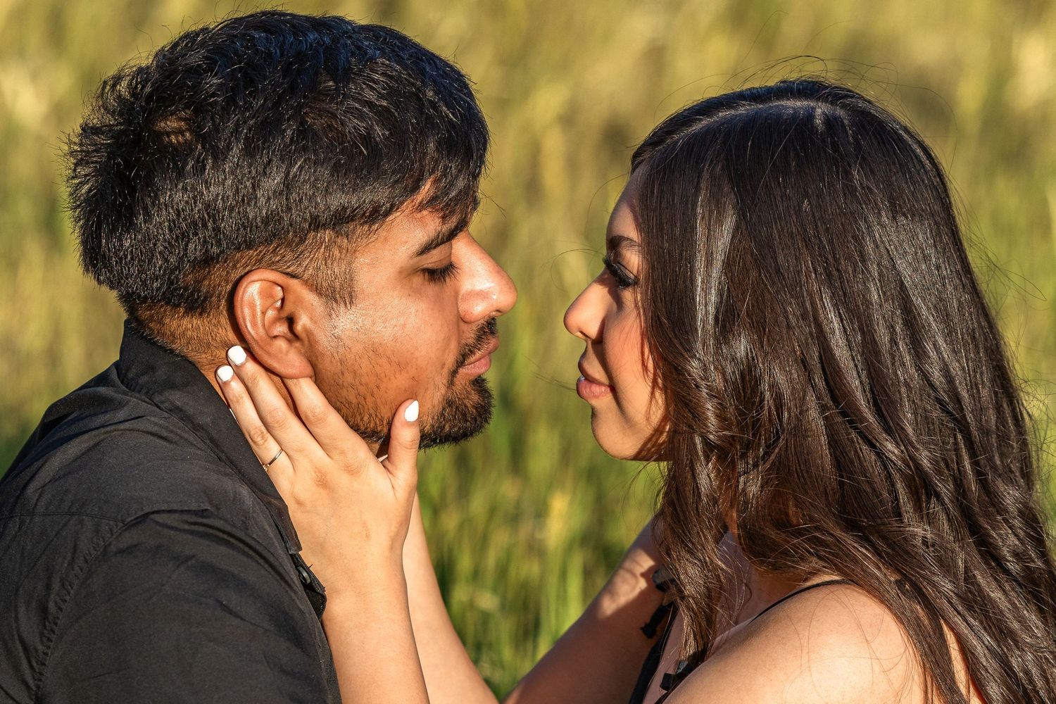 A romantic couple sharing an intimate moment outdoors, with the woman tenderly holding the man's face close to hers.