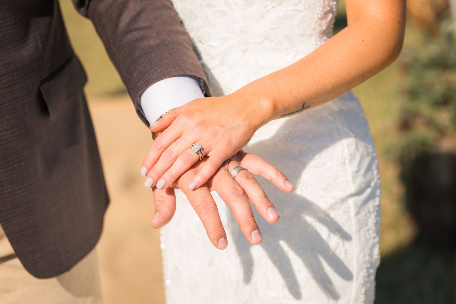 Newlywed couple displaying wedding rings on their hands, bride in white lace dress and groom in gray suit.