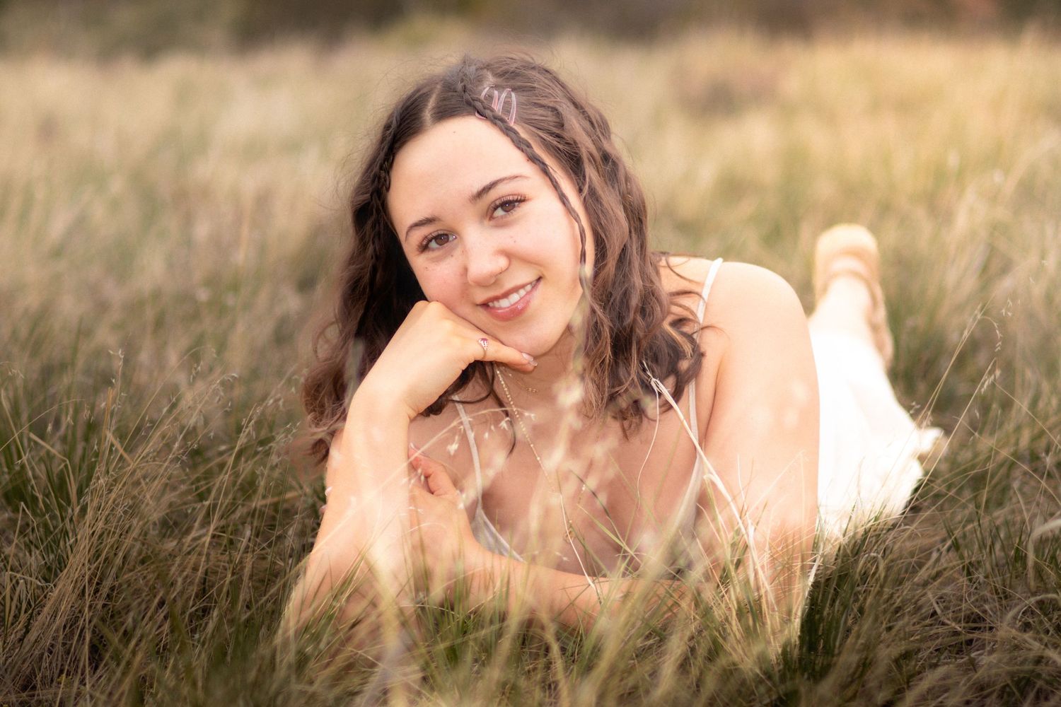 Young woman with curly hair smiling while lying in a golden grass field outdoors in Littleton, Colorado.