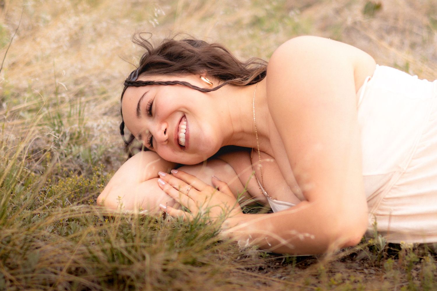 Woman laughing joyfully while lying in a grassy field wearing a white dress in Littleton, Colorado.
