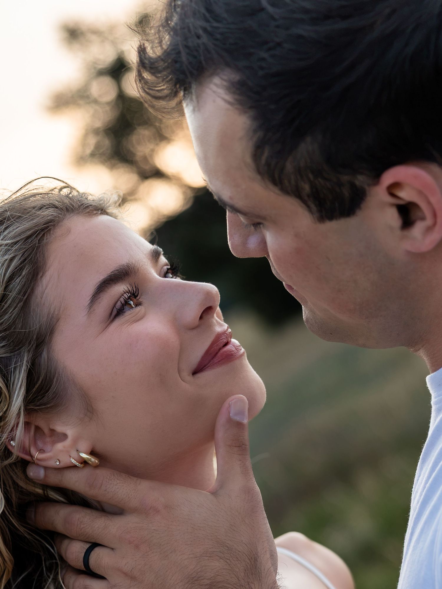 A romantic couple shares an intimate moment outdoors, with golden backlight as the man tenderly holds the woman's face.