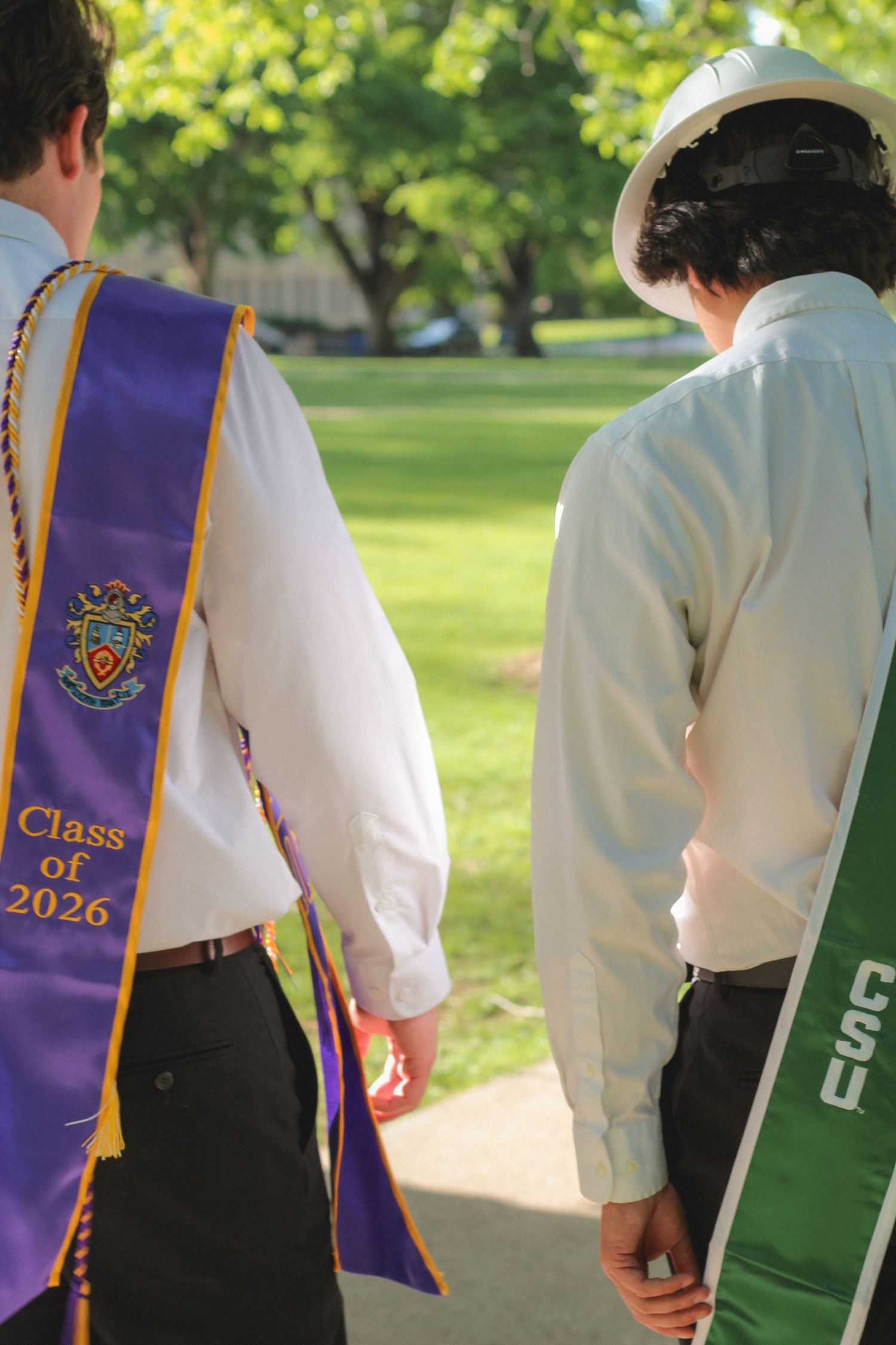 Two graduates walking outdoors wearing purple Class of 2026 and green CSU graduation stoles.