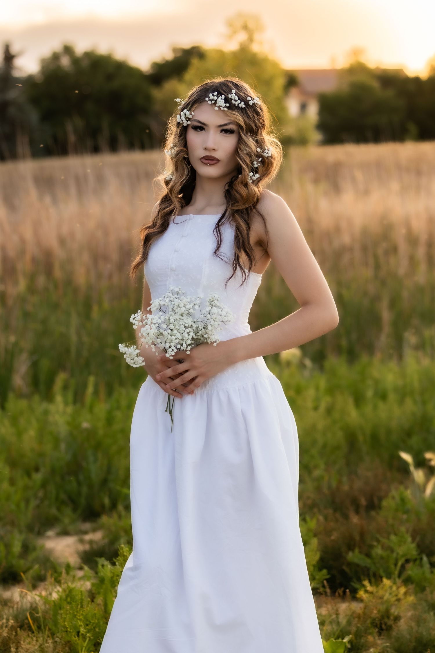 A beautiful bride in a white dress holds wildflowers wearing a floral crown in a golden sunset field in Littleton, Colorado.