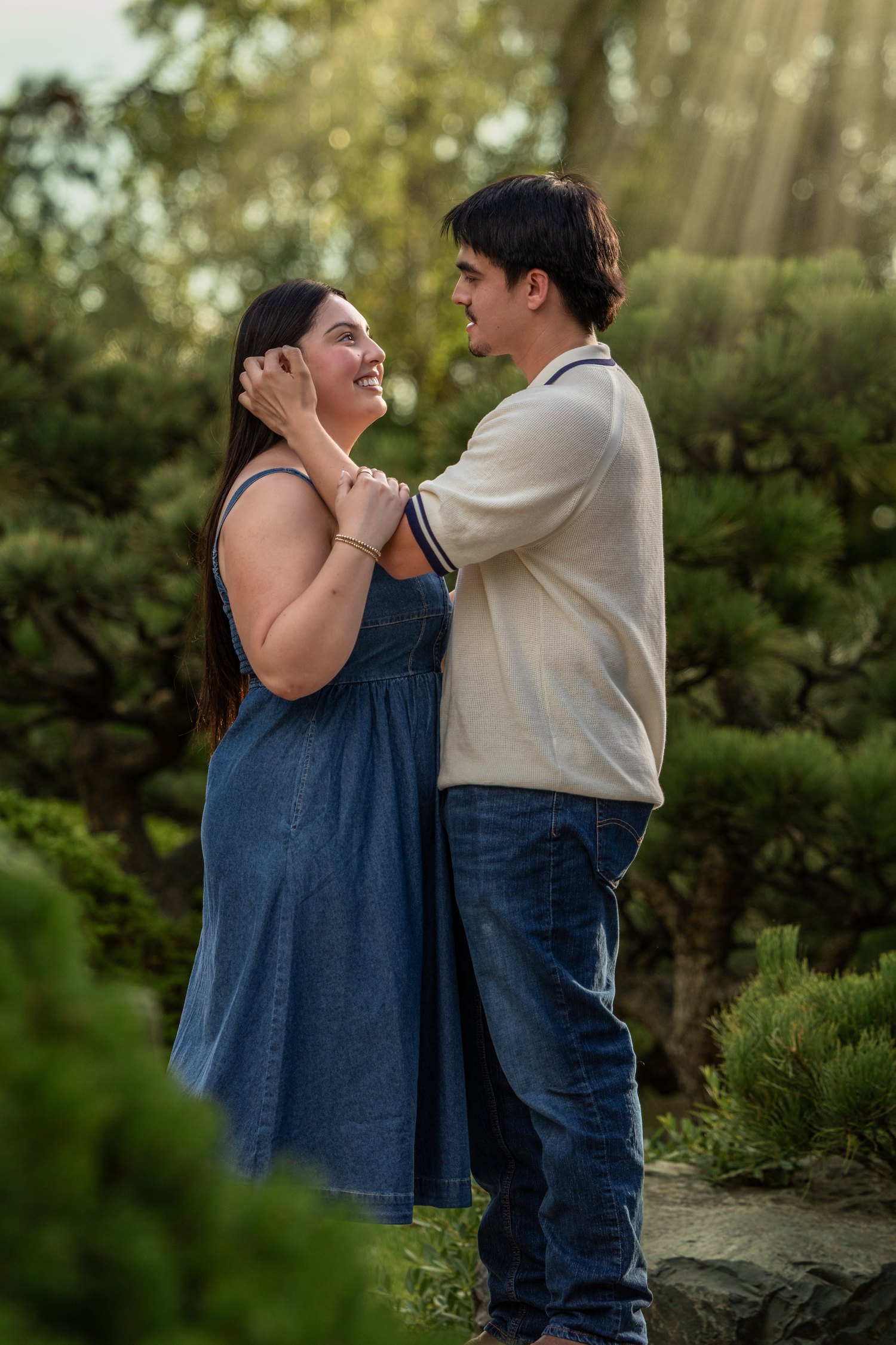 A couple shares a tender moment in a lush garden, the man gently touching the woman's face as she smiles up at him.
