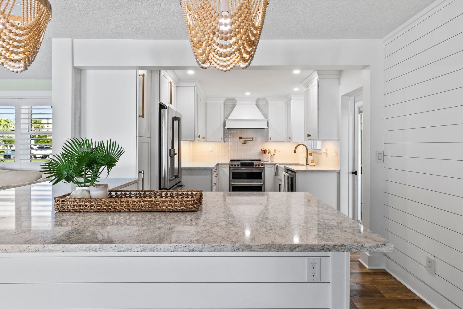 Modern farmhouse style kitchen features shiplap walls, quartz countertops and woven pendant lights over a white island.