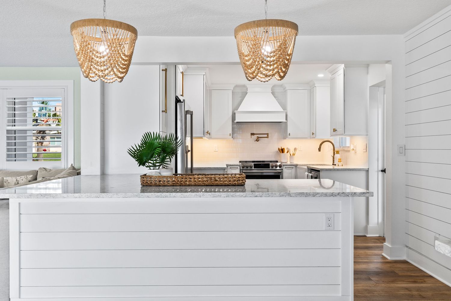 Modern white coastal kitchen with marble countertops, beaded chandeliers, and shiplap walls features high-end appliances.