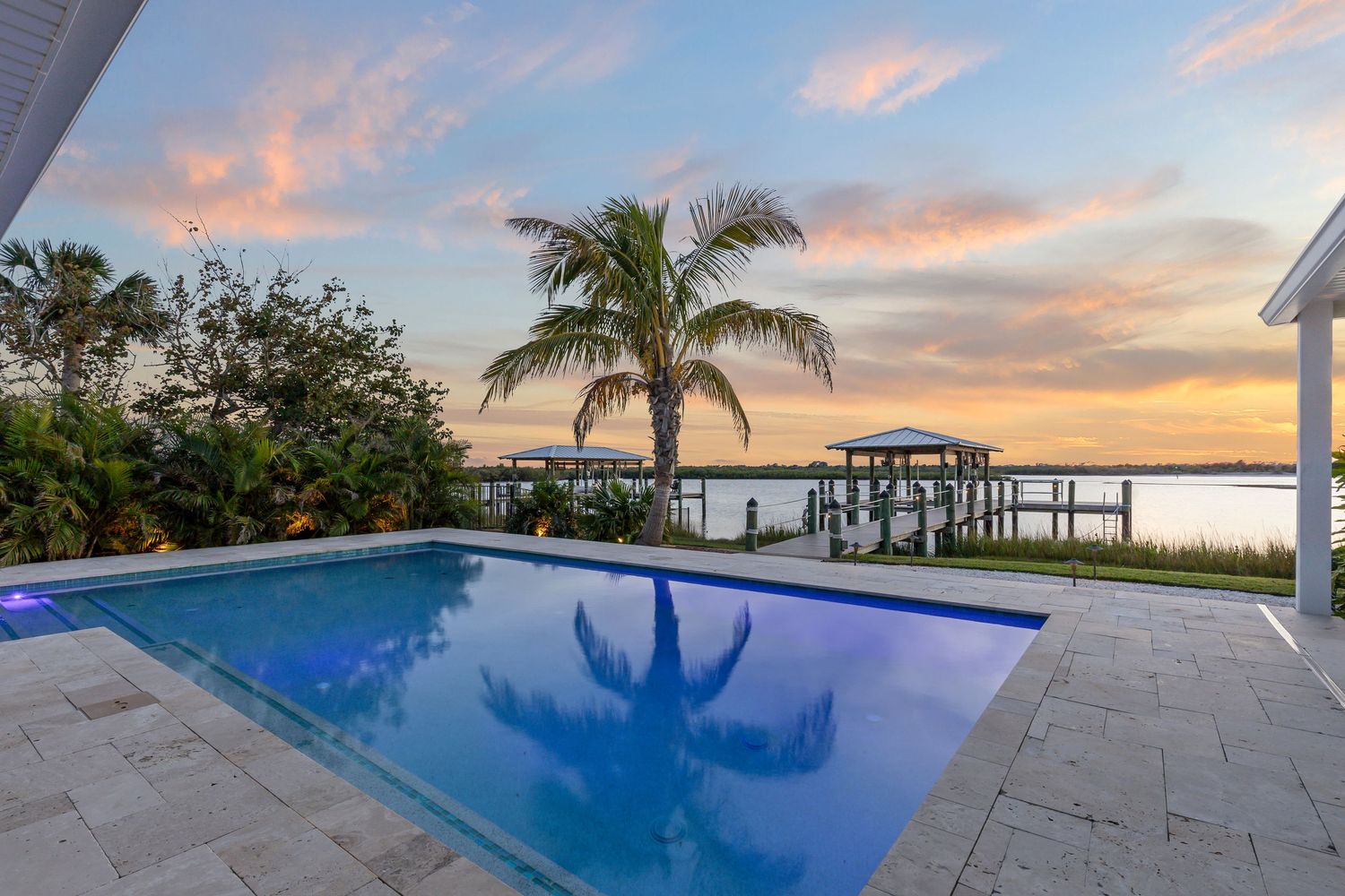 Luxurious waterfront pool with palm tree and private dock at sunset creating a stunning coastal Florida ambiance.