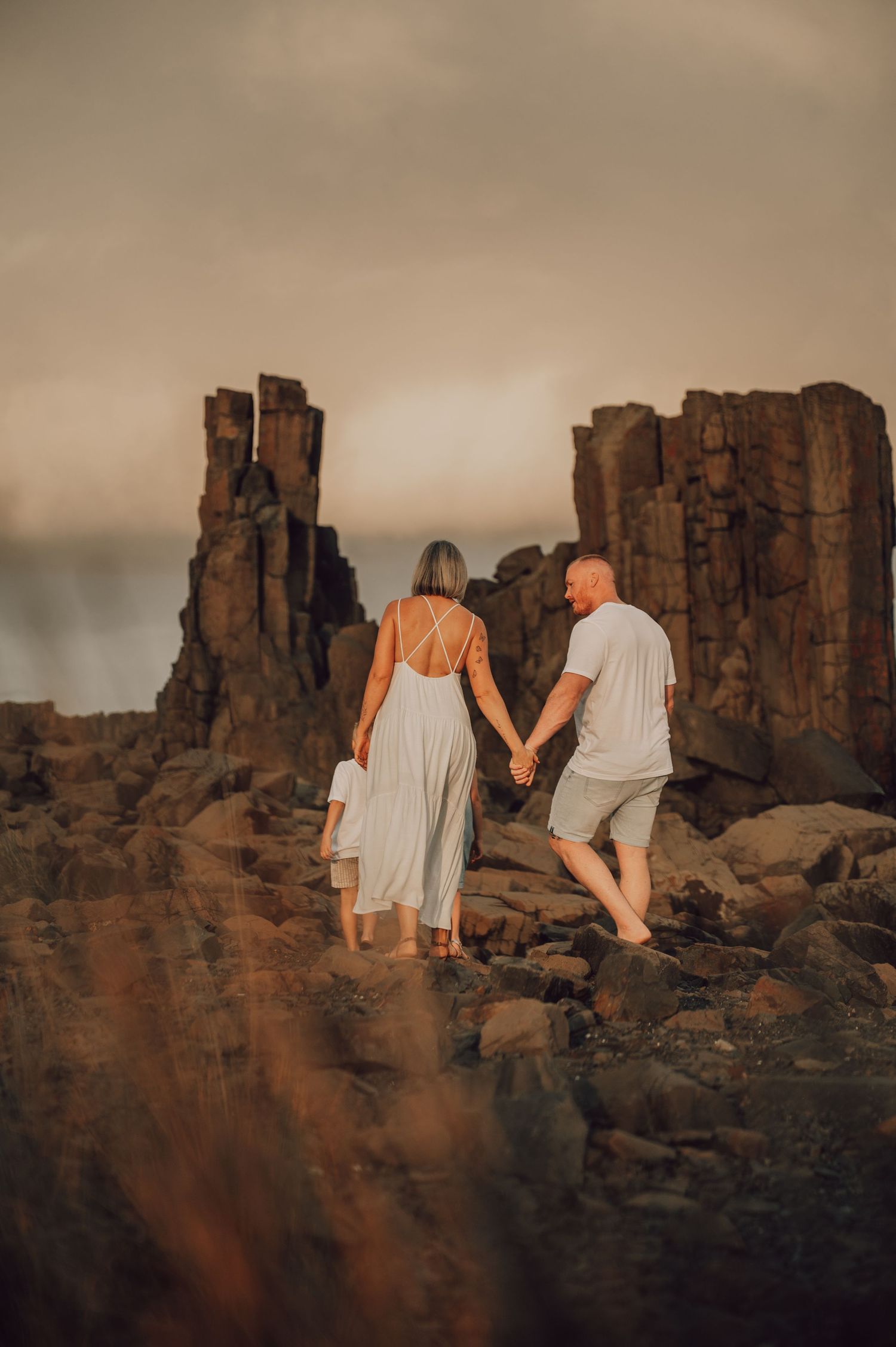 Couple holding hands walking among dramatic rock formations at moody coastal sunset. Family Photography