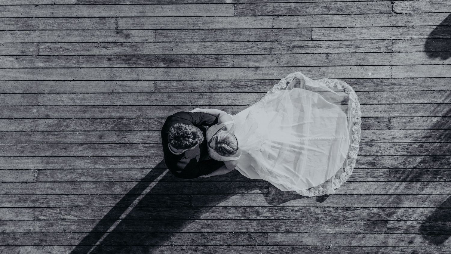 Aerial black and white view of bride and groom embracing on wooden deck. Wedding Photography.