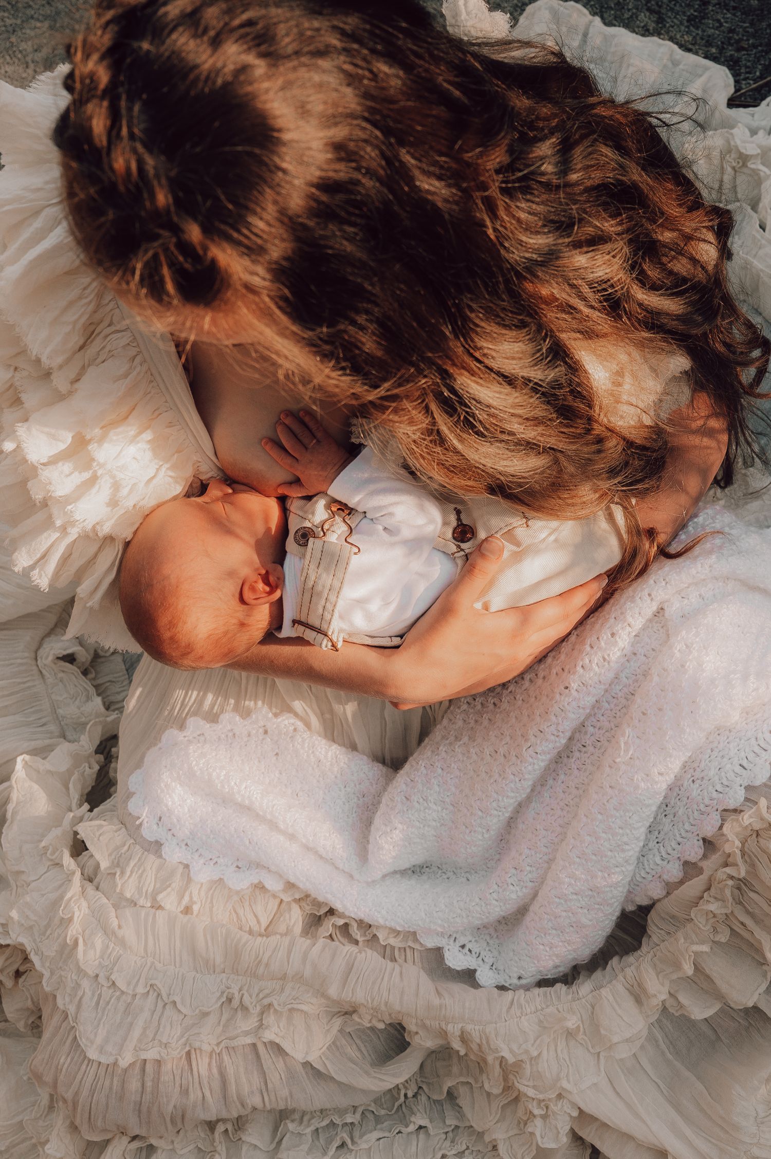 Mother tenderly kissing newborn baby wrapped in white lace blanket, overhead view. Newborn Photography
