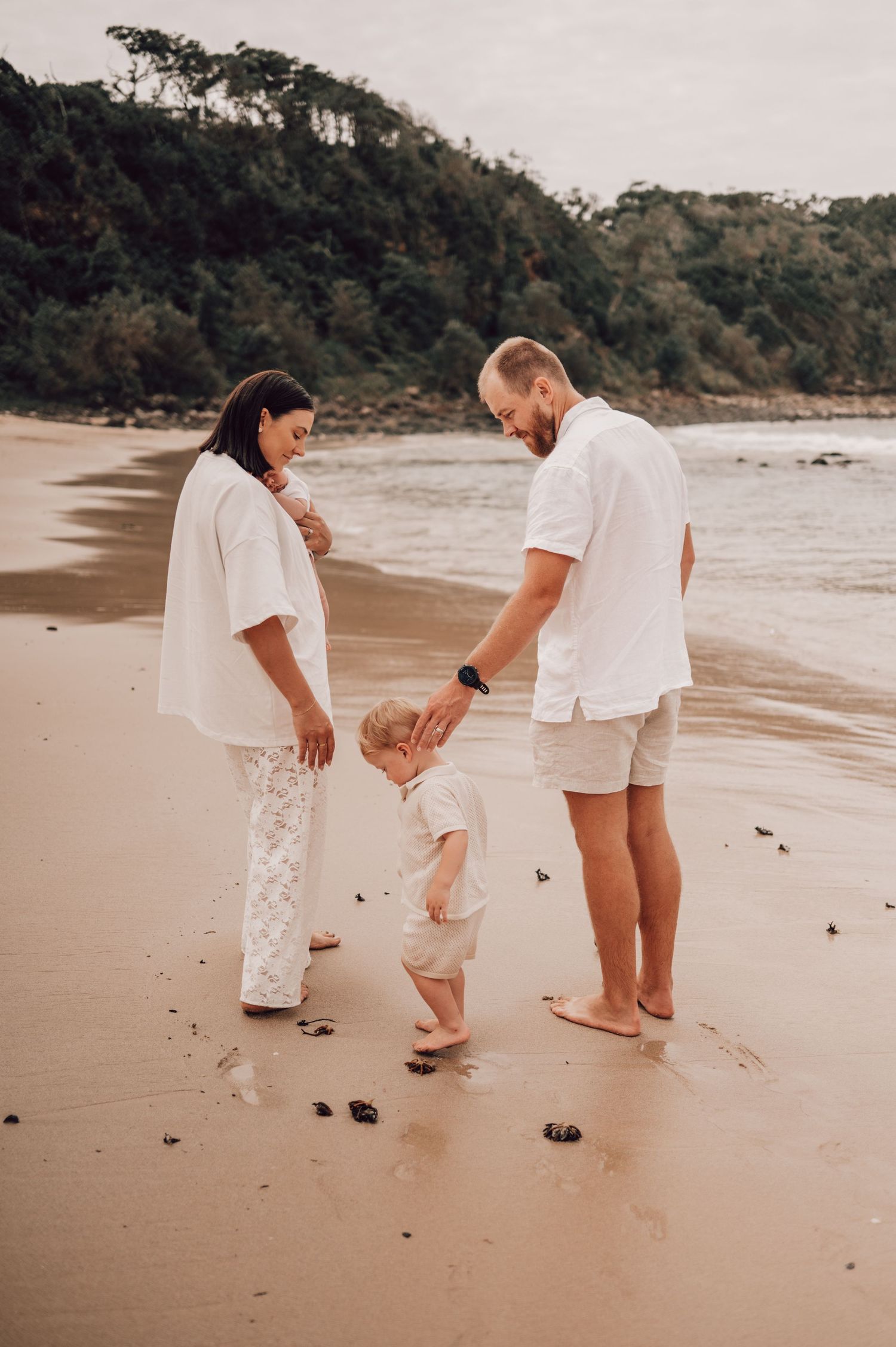 Young family with toddler enjoying a peaceful moment on sandy beach shore in matching white outfits. Family Photography