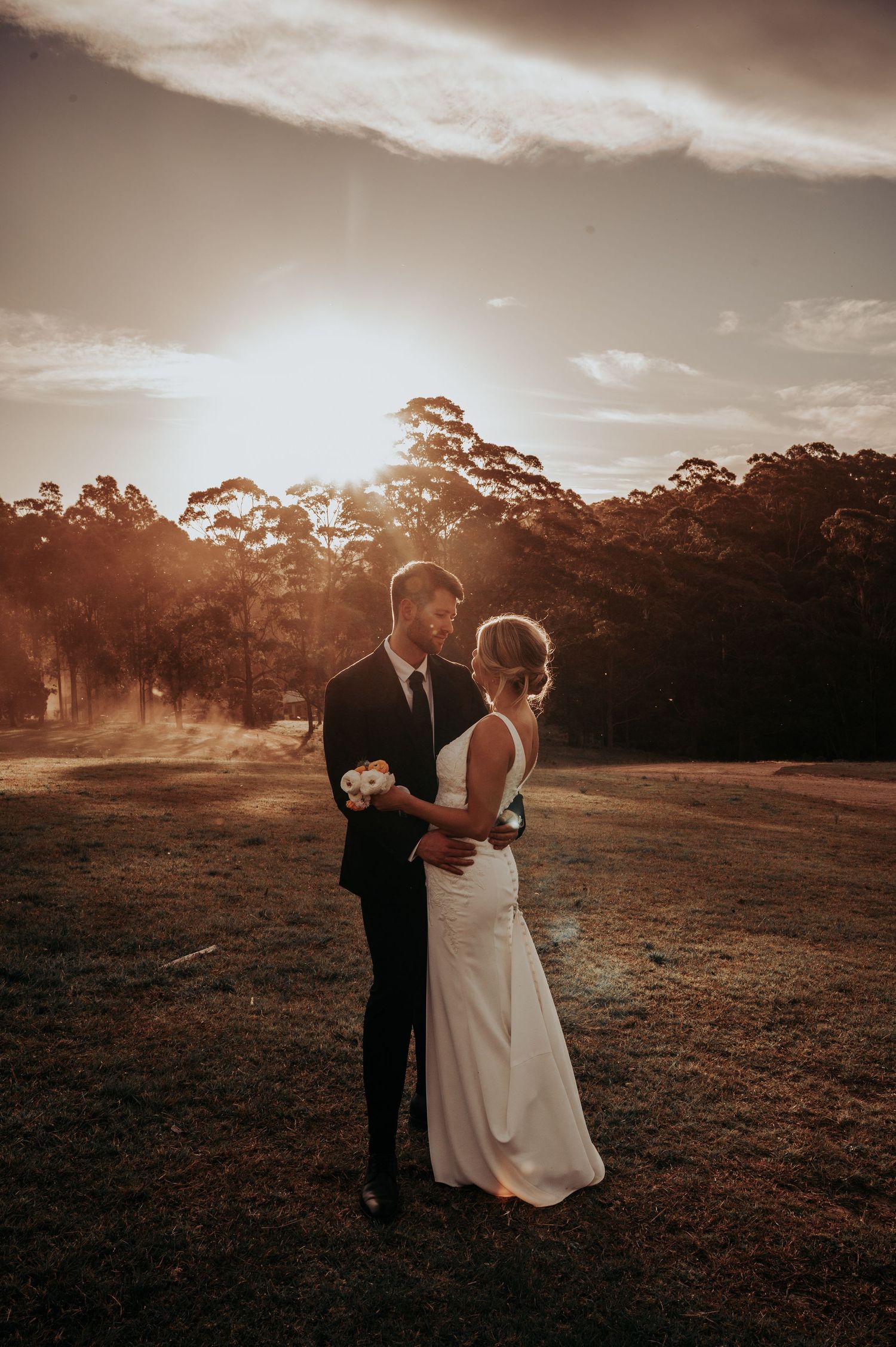 Bride and groom share a romantic moment at sunset in a field, with golden light and trees in the background. Wedding, wedding photography